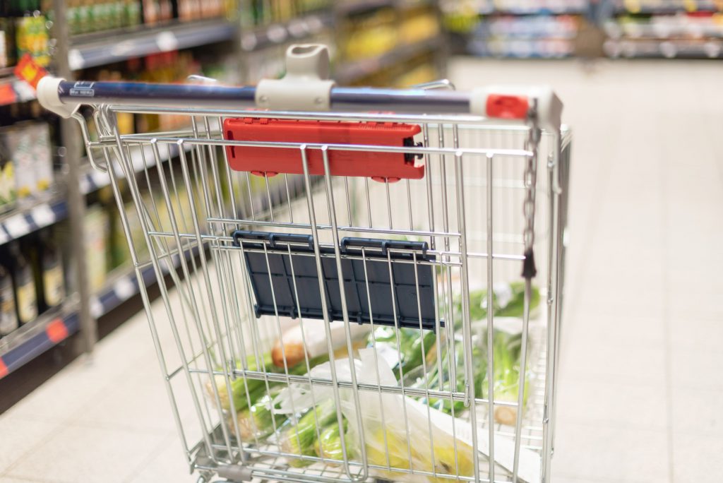 Grocery shopping cart full with food at blurred supermarket background. Copy space. Sustainable