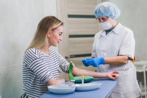 Preparation for blood test with beautiful young blond woman by female doctor in white coat medical